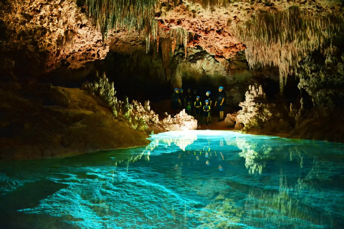 Illuminated cave passage with stalactites reflected in still water at Río Secreto on a cenote tour from Playa del Carmen, Mexico